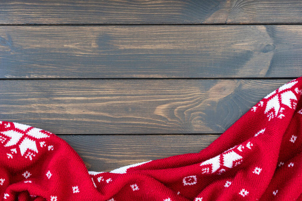 knitted red blanket with traditional christmas pattern with snowflakes lie crumpled on dark wooden background. Copy space for text. - Photo, Image