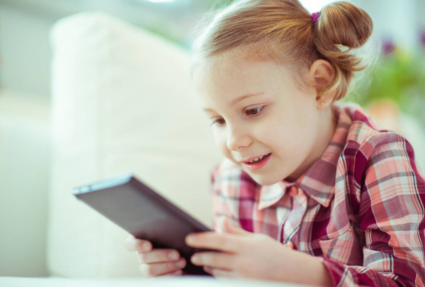 Portrait of cute little child girl laying on sofa with tablet at digital homeschooling - Foto, immagini