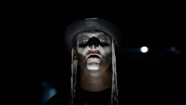 Zlověstný muž s kostrbatým make-upem se vynořuje ze tmy, když na něj dopadne světlo a dělá obličeje - Záběry, video