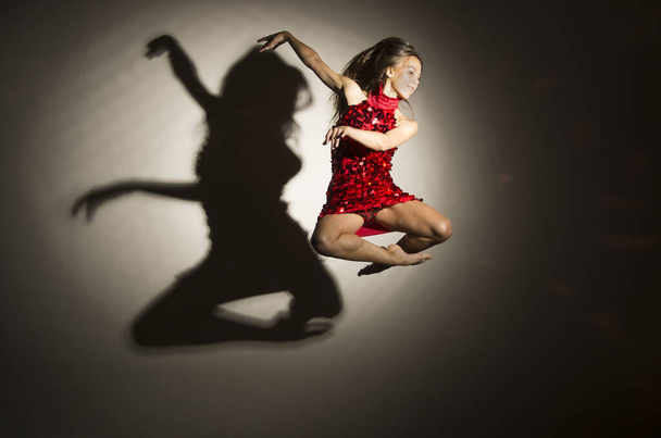 A girl in a red dress performs gymnastic jumps, a shadow from a figure appears on a white background. Studio photography. - Foto, afbeelding