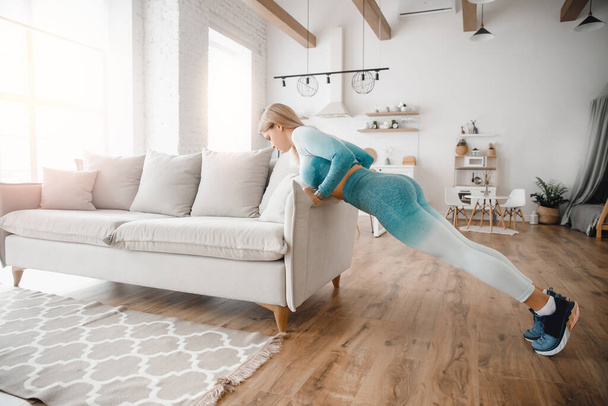 Стройная спортивная женщина делает упражнения на прессе на домашней кухне с диваном - Фото, изображение
