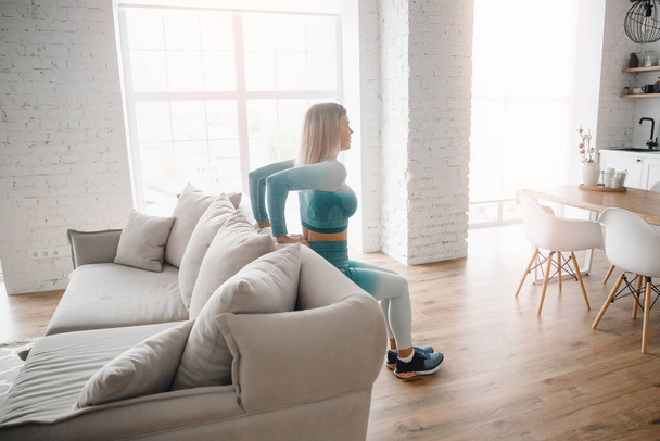Slim σπορ κορίτσι κάνει push-up ασκήσεις με αυτοσχέδια αντικείμενα καναπέ στο σπίτι. Concept Lifestyle σπορ για πανδημία - Φωτογραφία, εικόνα