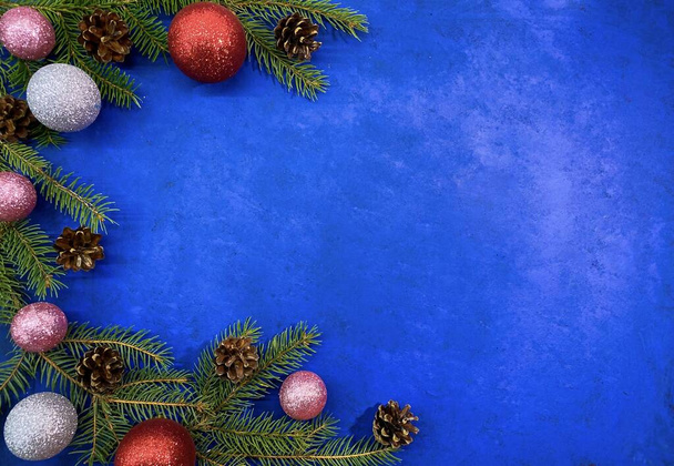 Heller weihnachtlicher Hintergrund. Tannenzweige mit Tannenzapfen und Kugeln auf einer abstrakten blauen Oberfläche. Blick von oben, Kopierraum. - Foto, Bild