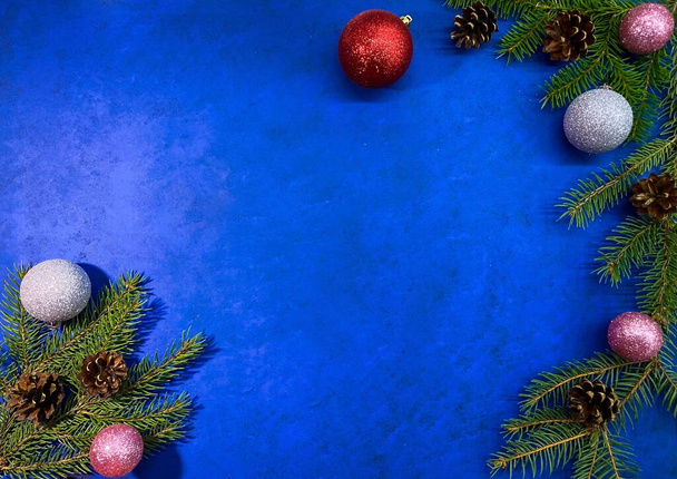 明るいクリスマスの背景。抽象的な青色の表面に松コーンとボールを持つモミの枝。上部からの表示、スペースのコピー. - 写真・画像