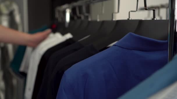 Un homme passe sa main sur des T-shirts suspendus à un cintre dans un magasin close-up. Magasin de vêtements. - Séquence, vidéo
