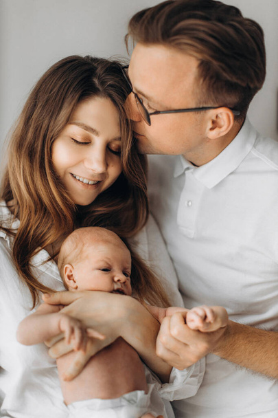 Happy parents with newborn baby girl, loving mother hold little daughter in arms, caring husband kiss gorgeous wife, enjoy happy moments, young family concept - Fotoğraf, Görsel