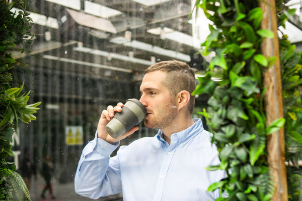Photo of a young and attractive business man wearing smart casual clothes enjoying a cup of coffee in a reusable cup during a job break. Smart working environment - Fotoğraf, Görsel