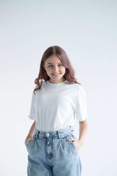 Ritratto di bella adolescente in t-shirt bianca e jeans blu in posa con le mani in tasche su sfondo grigio studio. - Foto, immagini
