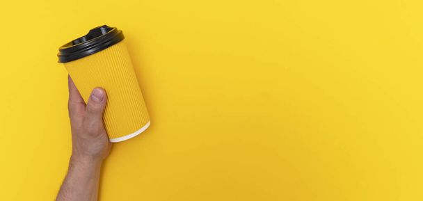 Coffee takeaway in yellow paper cup with black lid in left caucasian is yellow background - Foto, afbeelding