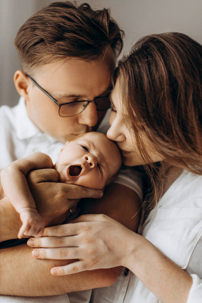 Happy parents with cute newborn baby girl, handsome dad hold little daughter in arms, beautiful wife and loving husband gently kiss their child, young family concept - Foto, immagini