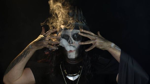 Sinistre homme avec Halloween squelette maquillage expirant cigarette fumer de sa bouche et souriant - Photo, image