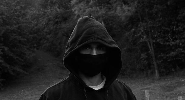junger Mann mit Maske und Kapuze in einem Park - Foto, Bild