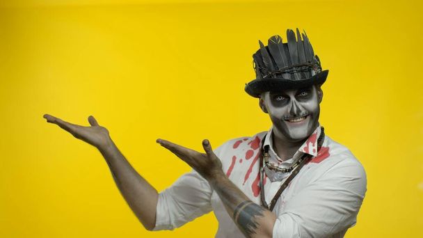 Sinister man with horrible Halloween skeleton makeup trying to scare, pointing to the left - Photo, Image