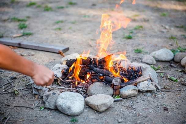 Burning forest at night. Campfire in a tourist camp outdoors in the mountains. Flame and fire sparks on a dark abstract background. We are preparing an outdoor barbecue. Infernal element of fire. Fuel, power and energy. Bonfire by the water in the fo - Photo, Image