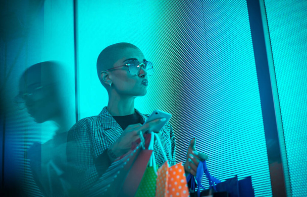 Image of a beautiful young woman posing against a led panel. Shaved head teenager with alternative look making urban portraits - Foto, afbeelding