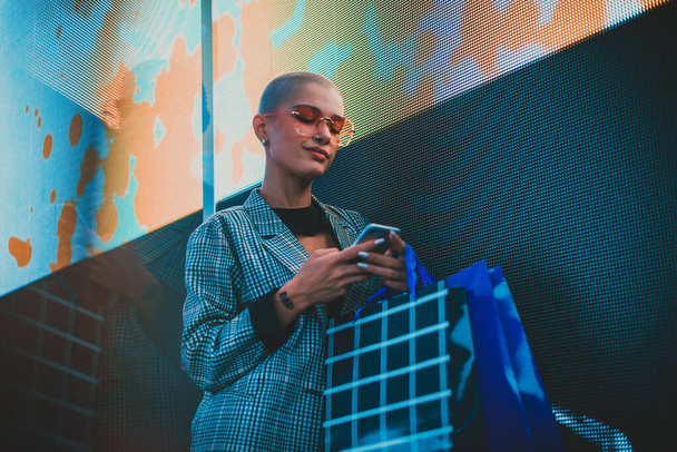 Image of a beautiful young woman posing against a led panel. Shaved head teenager with alternative look making urban portraits - Foto, Bild