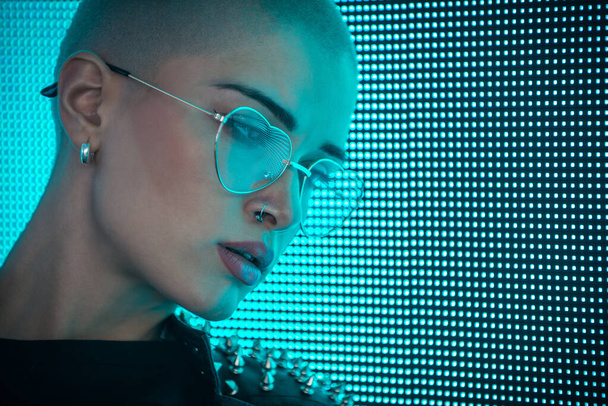 Image of a beautiful young woman posing against a led panel. Shaved head teenager with alternative look making urban portraits - Fotó, kép