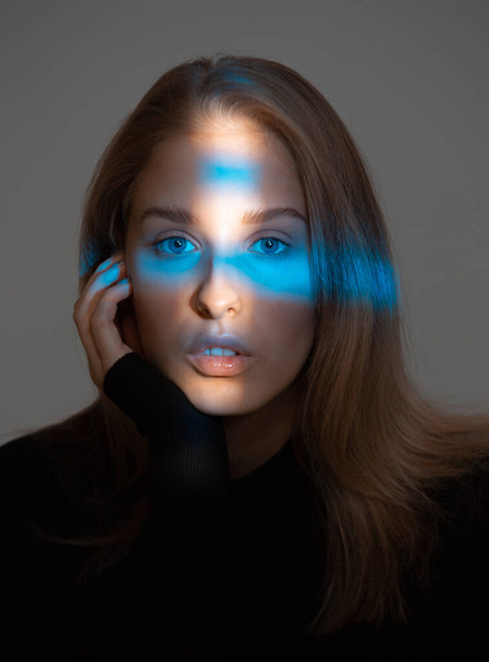 Portrait of young pretty female with ideal skin and blue neon light on face on gray studio background - Valokuva, kuva