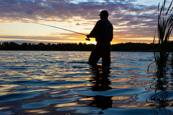 Silhouette of angler catching the fish durring sunset - Photo, Image