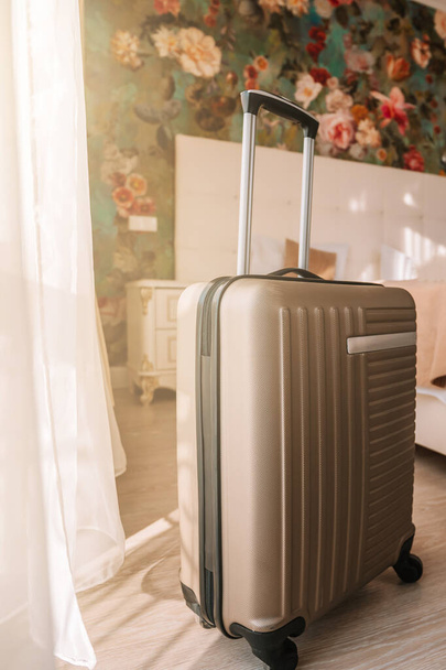 Туристична валіза стоїть у білій чистій кімнаті готелю зі світлом від вікна, розслаблюючим часом, святом, вихідними та концепцією подорожей
. - Фото, зображення