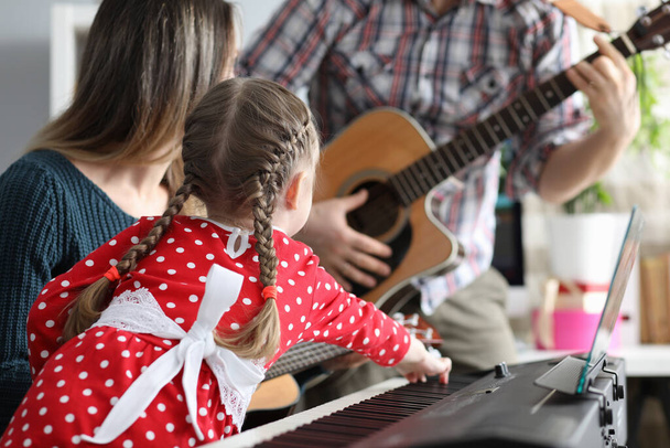 A lány, apa és anya együtt játszanak hangszeren, gitáron, pioninón. - Fotó, kép