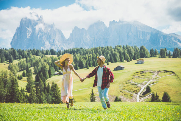 Happy couple on vacation on the italian dolomites mountains. Young man and woman making activities on a beautiful green meadow - Foto, afbeelding
