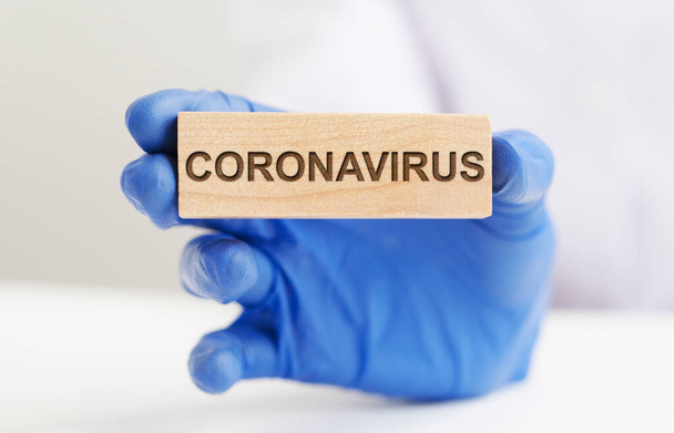 Coronavirus COVID word on wooden block in hand of doctor in blue protective glove. white background. - Foto, immagini