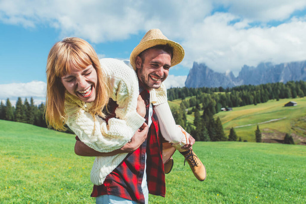 Happy couple on vacation on the italian dolomites mountains. Young man and woman playing together on the green meadow - Fotografie, Obrázek