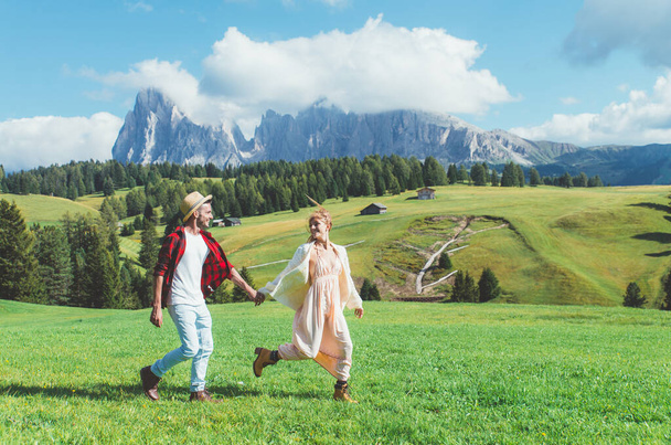 Happy couple on vacation on the italian dolomites mountains. Young man and woman playing together on the green meadow - Foto, Imagen