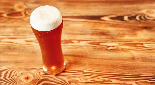 Μακρύ ποτήρι φρέσκιας μπύρας με αφρό σε ξύλινο πάγκο μπαρ, σκούρο φόντο - Φωτογραφία, εικόνα