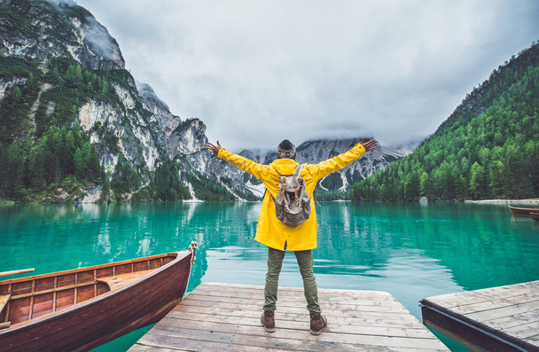 Mountain stories. Happy backpacker on a wanderlust vacation. Man with a yellow raincoat standing in front the lake and enjoying the view - Фото, изображение