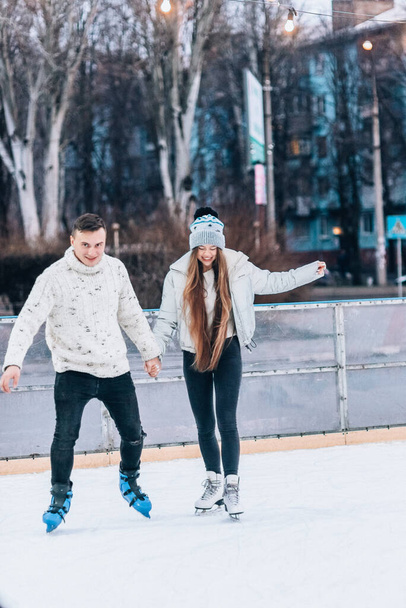Lächelndes junges Paar beim Eislaufen im Freien mit Schnee im Hintergrund - Foto, Bild