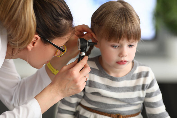 Kadın otorhinolaryngolog klinikte otoskopla küçük kızların kulaklarını inceliyor. - Fotoğraf, Görsel