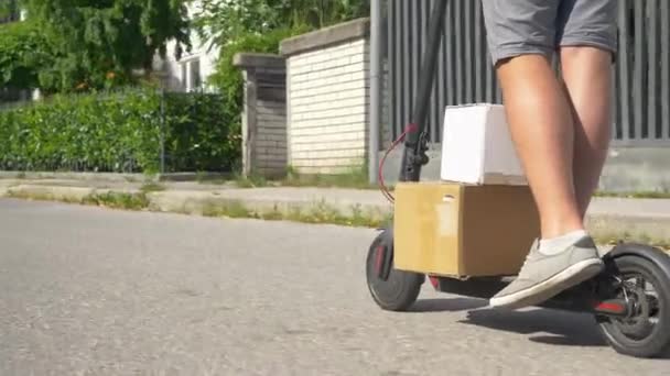 LOW ANGLE: Unrecognizable courier transports two cardboard boxes on e-scooter. - Footage, Video