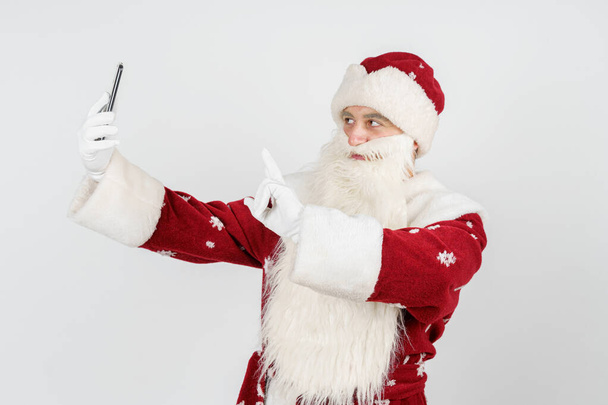 Noel et Nouvel An concept. Le Père Noël pose, fait un selfie sur un téléphone portable. Contexte isolé - Photo, image