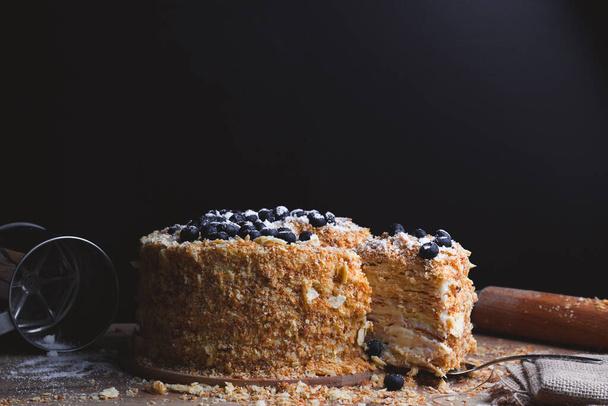 Gâteau Napoléon avec les bleuets à côté des ustensiles de cuisine sur le fond noir avec espace de copie. - Photo, image