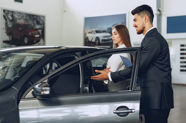 Man car dealer showing a woman buyer a new car - Foto, afbeelding