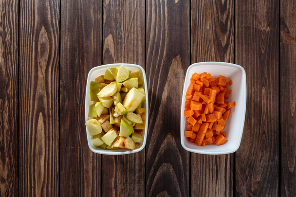 making carrot applesauce. two white bowls with chopped vegetables and fruits on the table. diced dice in a bowl. apples, peeled and diced in a white bowl. - Foto, afbeelding