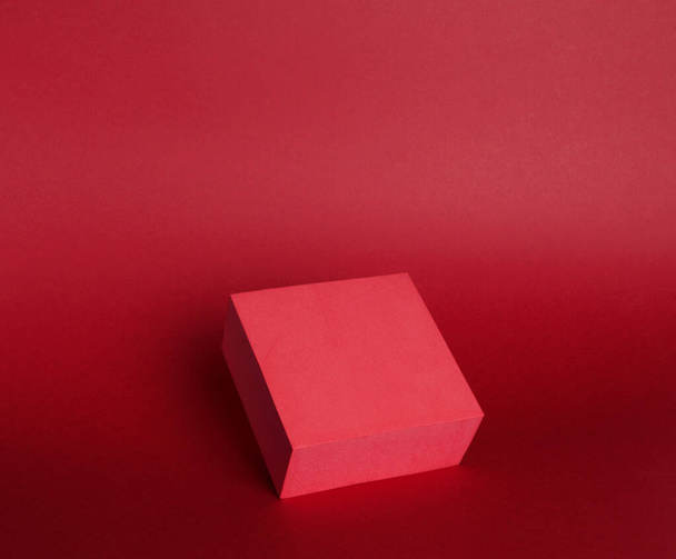 Fénykép egy fényes dobogón (talapzat) egy kocka egy papír alapon. Piros színnel, lejtővel és árnyékkal. Reklámhely. Üres termék stand és elvont háttér. - Fotó, kép