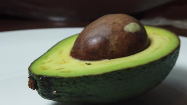 Половина авокадо на белой тарелке - Кадры, видео