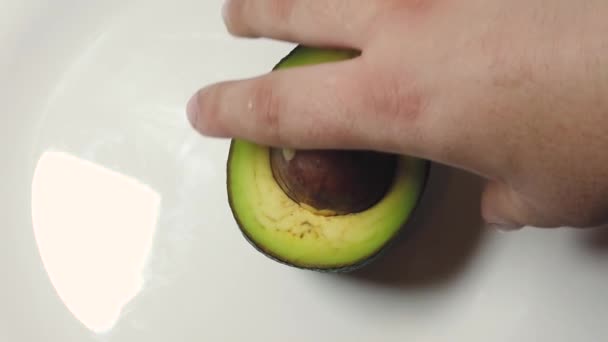 Hand spinnen avocado op de witte plaat. Langzame beweging - Video