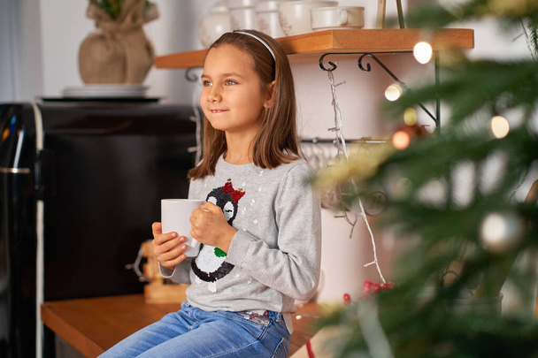 A little girl with a cup of hot tea dreams of a Santa present for Christmas. - Foto, imagen