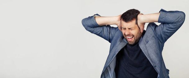 Young businessman man with a beard in a jacket. Hands on head, suffering from headache in despair and under stress due to pain and migraine. Portrait of a man on a gray background. - Foto, afbeelding