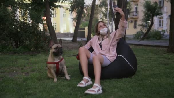 Όμορφη νεαρή γυναίκα βγάζει selifie με το γαλλικό μπουλντόγκ της στο πάρκο - Πλάνα, βίντεο