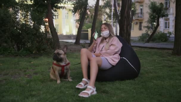 Fiatal nő ül a babzsák szék a francia bulldog és beszél telefonon - Felvétel, videó
