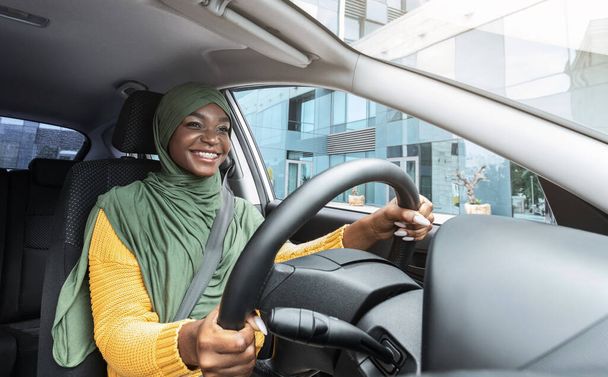 Βόλτα. Ευτυχισμένο χαμόγελο μαύρο μουσουλμάνα κυρία με μαντίλα οδήγηση σύγχρονο αυτοκίνητο - Φωτογραφία, εικόνα