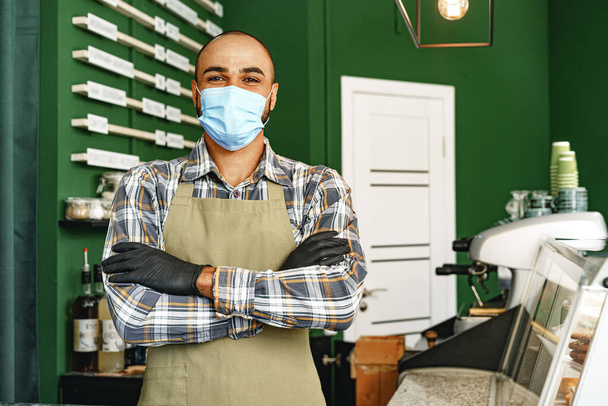 Coffee shop worker wearing medical mask while standing at counter in cafeteria - Foto, Imagem