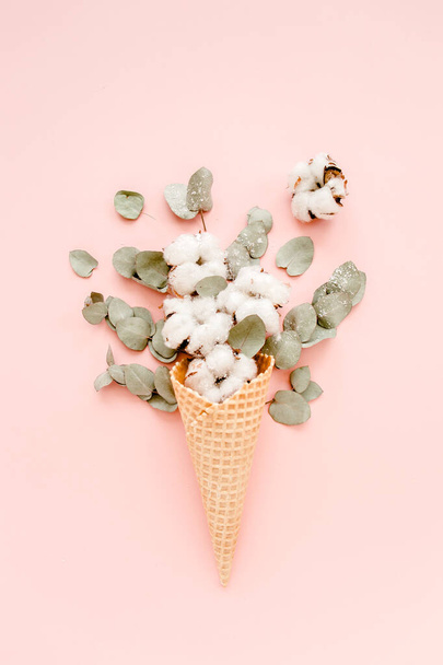 Waffle cone with cotton bouquet and eucalyptus leaves on pink background, flat lay, top view - Foto, Imagen