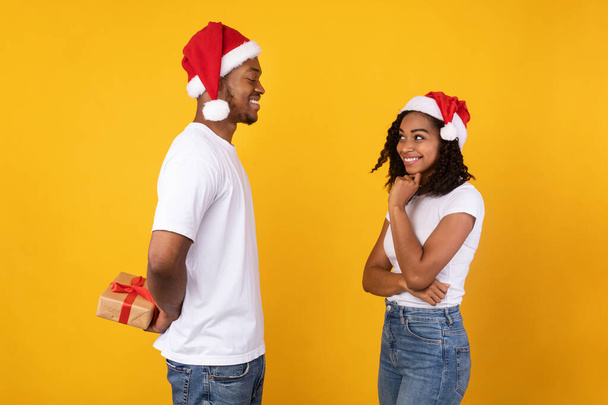 Hombre negro sosteniendo envuelto regalo de Navidad felicitando novia, fondo amarillo - Foto, Imagen