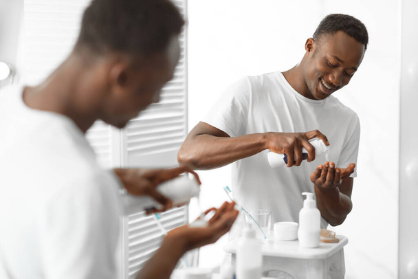 Afrikaner benutzt Rasierschaum, der in der Nähe von Spiegel im Badezimmer steht - Foto, Bild